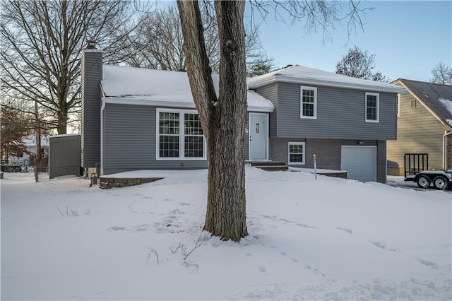 snow covered rear of property featuring a garage