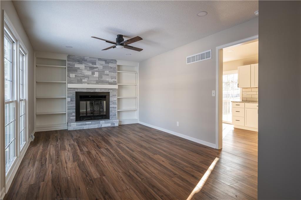 unfurnished living room with hardwood / wood-style floors, ceiling fan, a large fireplace, and built in features