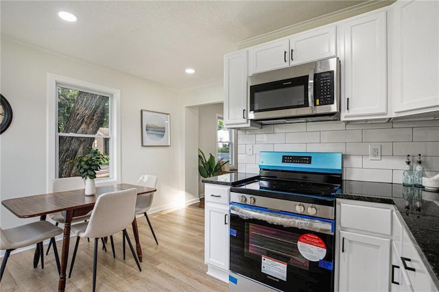 kitchen with dark stone counters, white cabinets, light wood-type flooring, and appliances with stainless steel finishes