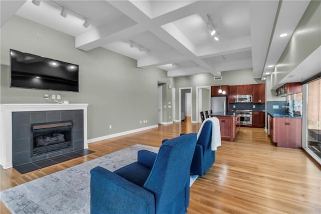 living room with a tiled fireplace, sink, rail lighting, and light hardwood / wood-style floors