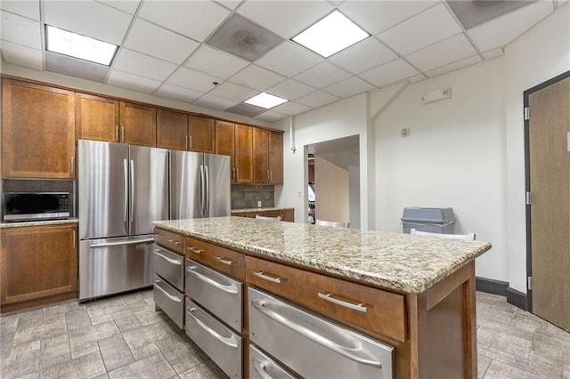 kitchen with decorative backsplash, appliances with stainless steel finishes, a paneled ceiling, light stone countertops, and a kitchen island