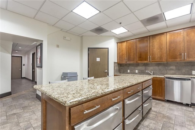 kitchen with dishwasher, decorative backsplash, a paneled ceiling, and light stone countertops