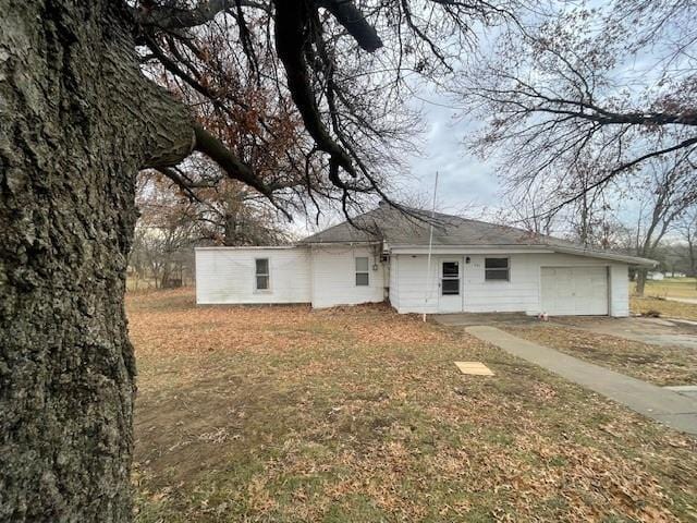 back of property featuring a garage, concrete driveway, and a yard