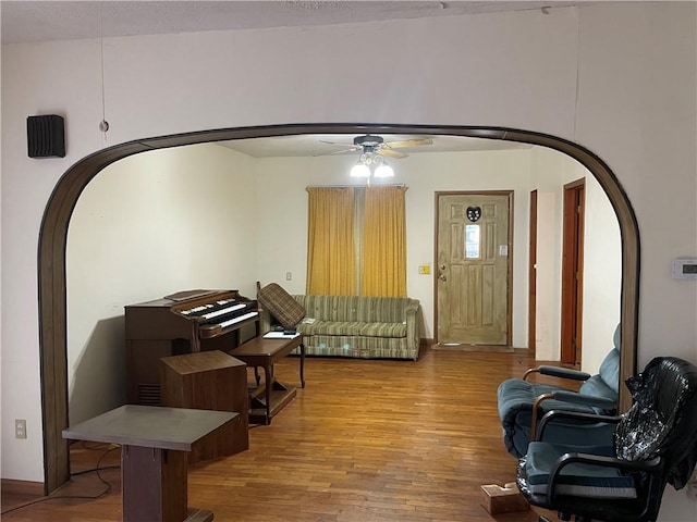 living area featuring a ceiling fan, arched walkways, and wood finished floors