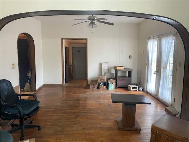 interior space featuring a ceiling fan, arched walkways, and dark wood-style flooring