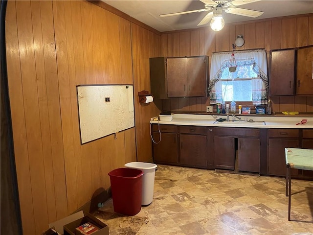 kitchen featuring ceiling fan, light countertops, wood walls, and a sink