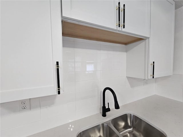 interior details featuring decorative backsplash, light stone countertops, sink, and white cabinets