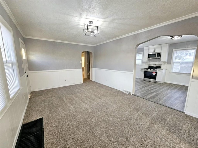 carpeted empty room with a textured ceiling, crown molding, and a notable chandelier