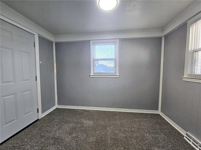 unfurnished bedroom featuring multiple windows, wood walls, and dark colored carpet