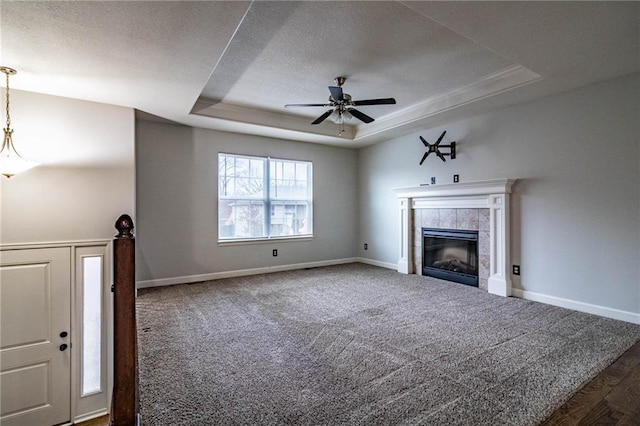 unfurnished living room with a tile fireplace, dark carpet, a raised ceiling, and ceiling fan