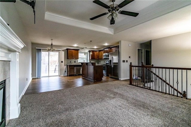 unfurnished living room with dark carpet, a tile fireplace, ceiling fan with notable chandelier, a raised ceiling, and crown molding