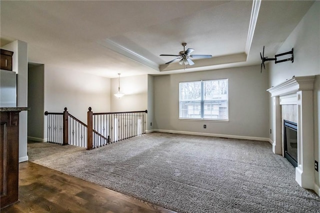 unfurnished living room featuring dark carpet, a raised ceiling, and ceiling fan