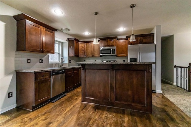 kitchen featuring appliances with stainless steel finishes, dark hardwood / wood-style flooring, sink, decorative light fixtures, and a center island