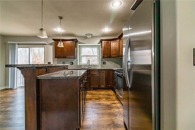 kitchen with appliances with stainless steel finishes, dark hardwood / wood-style flooring, sink, a center island, and hanging light fixtures