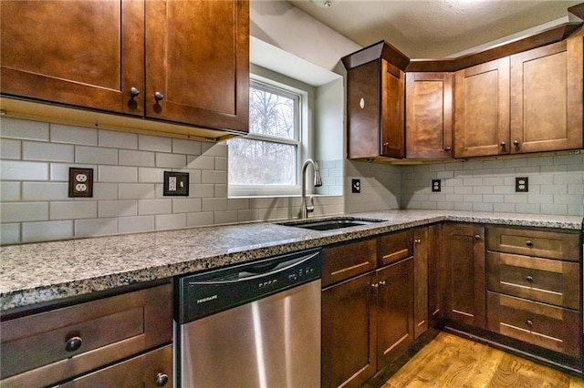 kitchen with light stone countertops, sink, tasteful backsplash, stainless steel dishwasher, and light wood-type flooring