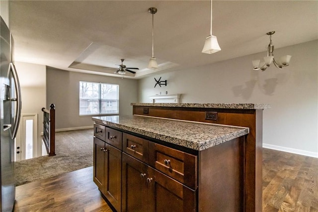 kitchen with stainless steel fridge, ceiling fan with notable chandelier, a raised ceiling, a kitchen island, and hanging light fixtures