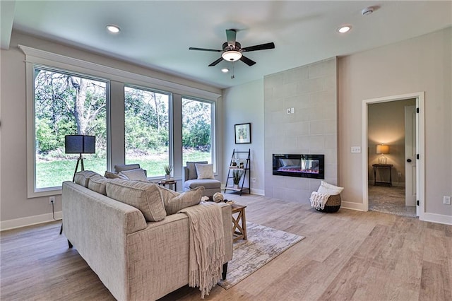 living room with a tiled fireplace, ceiling fan, and light hardwood / wood-style flooring