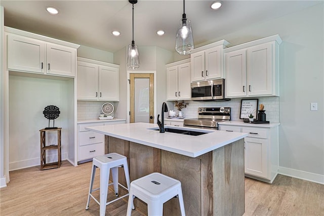 kitchen with a kitchen island with sink, pendant lighting, white cabinets, and stainless steel appliances