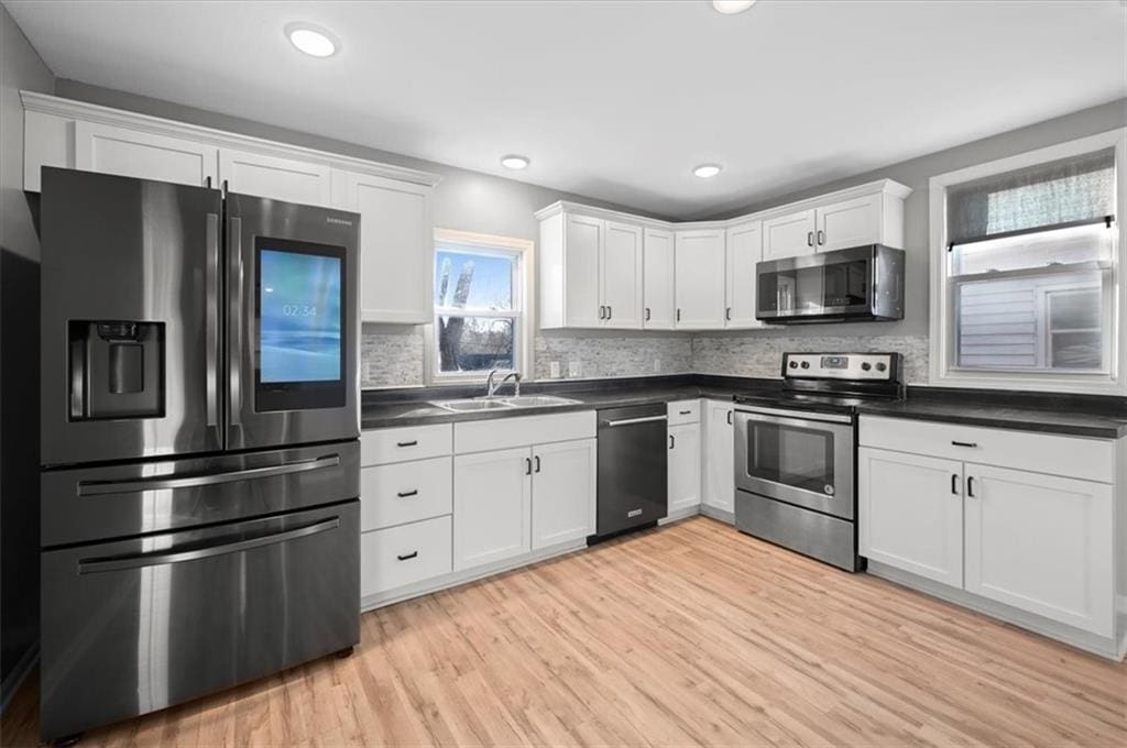 kitchen with sink, light hardwood / wood-style flooring, decorative backsplash, white cabinetry, and stainless steel appliances