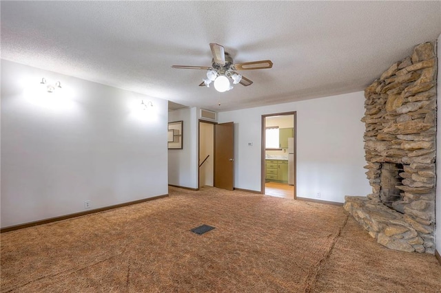 empty room featuring carpet flooring, a stone fireplace, ceiling fan, and a textured ceiling