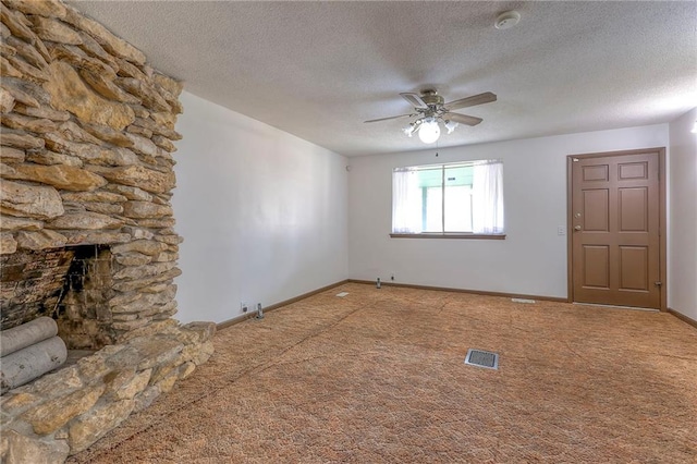 unfurnished living room featuring carpet, a textured ceiling, a stone fireplace, and ceiling fan