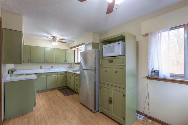 kitchen featuring a textured ceiling, green cabinets, white appliances, and light wood-type flooring