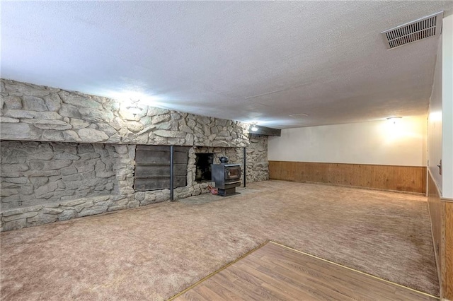 basement with hardwood / wood-style floors, wood walls, a wood stove, and a textured ceiling