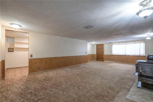 carpeted spare room with wood walls, a wood stove, and a textured ceiling