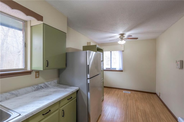 kitchen featuring stainless steel fridge, light wood-type flooring, a textured ceiling, ceiling fan, and green cabinetry