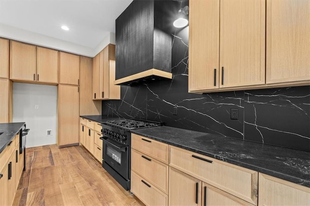 kitchen featuring tasteful backsplash, dark stone counters, high end stove, light brown cabinets, and light hardwood / wood-style flooring