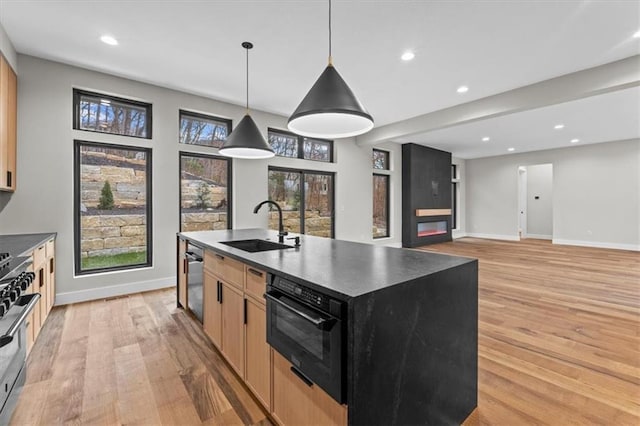 kitchen with light brown cabinets, sink, hanging light fixtures, an island with sink, and light hardwood / wood-style floors