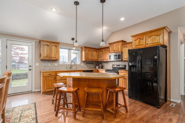 kitchen with lofted ceiling, light hardwood / wood-style flooring, decorative backsplash, appliances with stainless steel finishes, and a kitchen island