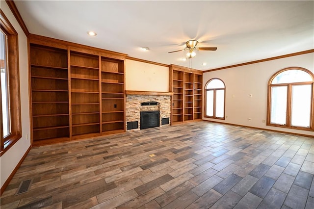 unfurnished living room with dark hardwood / wood-style flooring, a stone fireplace, ceiling fan, and crown molding