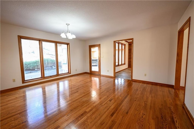 empty room featuring a chandelier, a textured ceiling, and hardwood / wood-style flooring