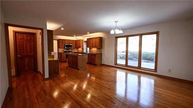 kitchen featuring dark hardwood / wood-style flooring, stainless steel appliances, pendant lighting, an inviting chandelier, and a center island