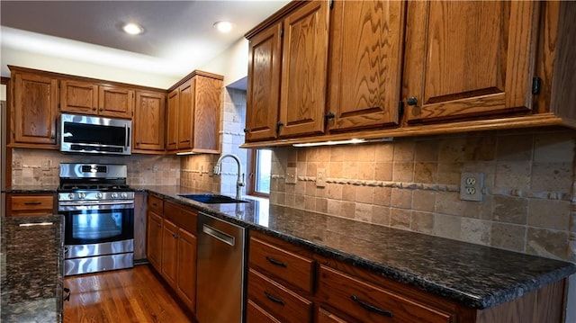 kitchen featuring sink, dark wood-type flooring, backsplash, dark stone countertops, and appliances with stainless steel finishes