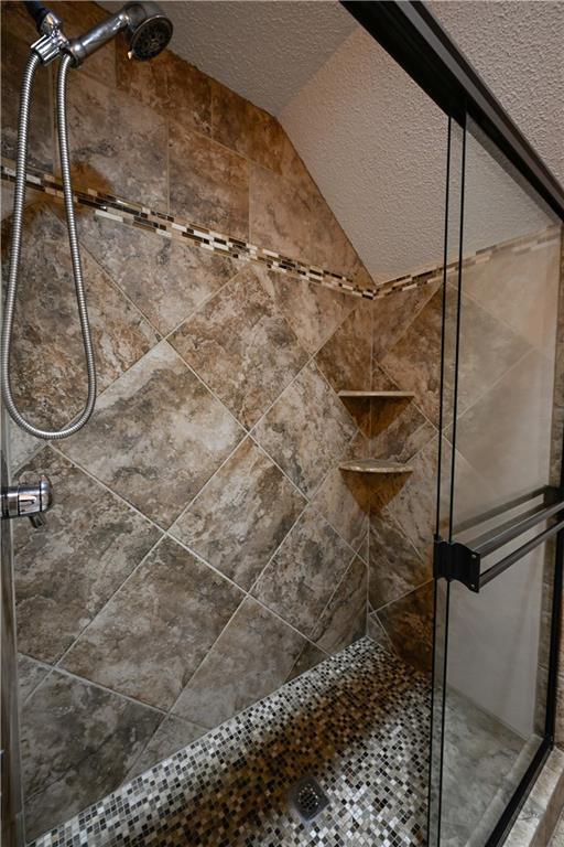 bathroom featuring a tile shower, a textured ceiling, and vaulted ceiling