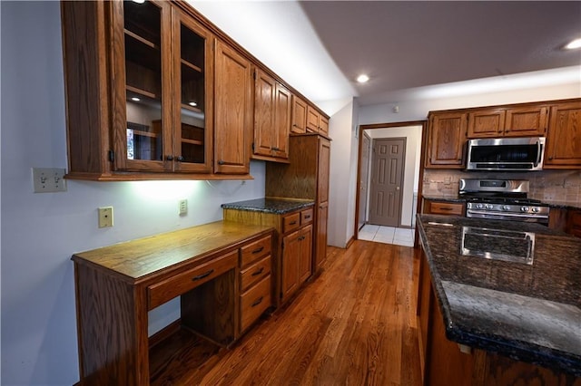 22812 E Bradford Ln, Blue Springs, MO 64015 - kitchen featuring appliances with stainless steel finishes, wood finished floors, tasteful backsplash, glass insert cabinets, and dark stone countertops