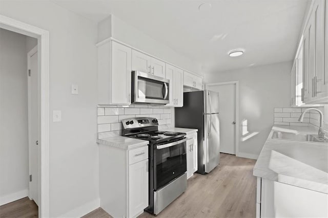 kitchen with appliances with stainless steel finishes, light wood-type flooring, backsplash, sink, and white cabinets