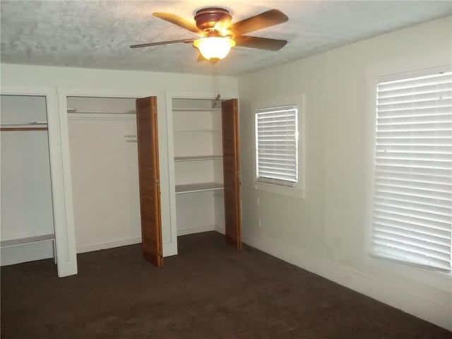 unfurnished bedroom featuring multiple closets, ceiling fan, and dark colored carpet