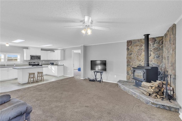 carpeted living room featuring ceiling fan, ornamental molding, a textured ceiling, and a wood stove