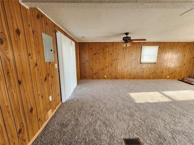 carpeted spare room with electric panel, ceiling fan, wooden walls, and a textured ceiling