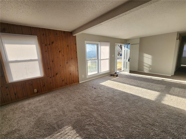 carpeted spare room featuring beam ceiling, wooden walls, and a textured ceiling