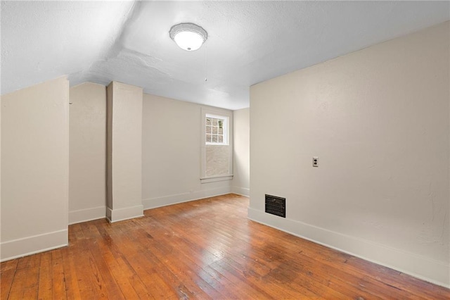 additional living space featuring lofted ceiling, wood-type flooring, and a textured ceiling