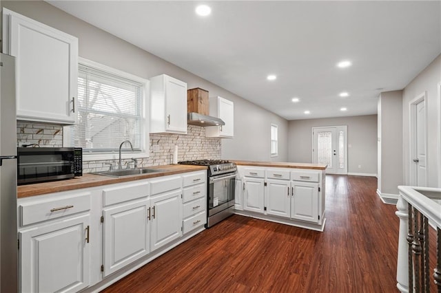 kitchen featuring a peninsula, a sink, under cabinet range hood, dark wood-type flooring, and appliances with stainless steel finishes