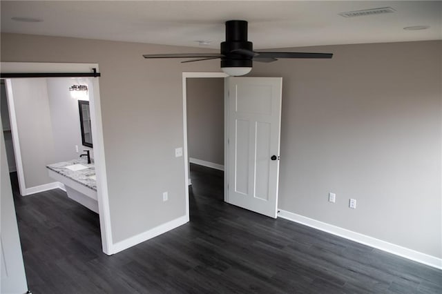 unfurnished bedroom with dark hardwood / wood-style floors, a barn door, and ceiling fan