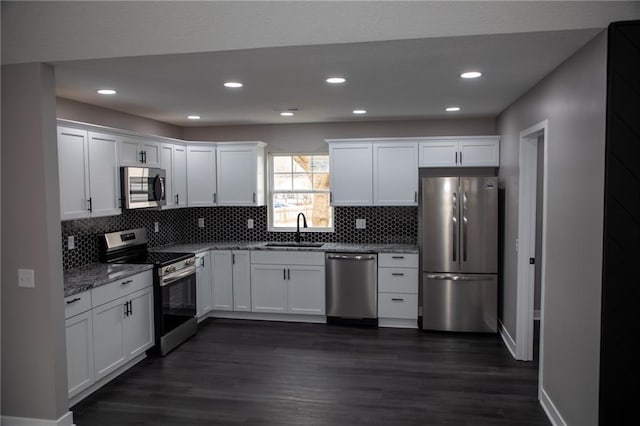 kitchen with appliances with stainless steel finishes, white cabinetry, sink, light stone counters, and dark wood-type flooring