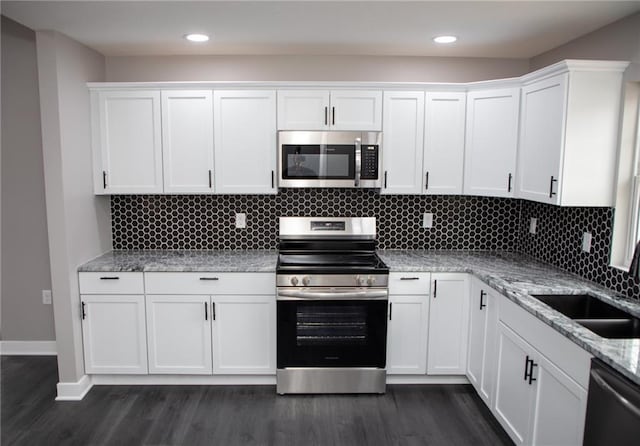 kitchen with sink, white cabinetry, stainless steel appliances, light stone countertops, and dark hardwood / wood-style flooring