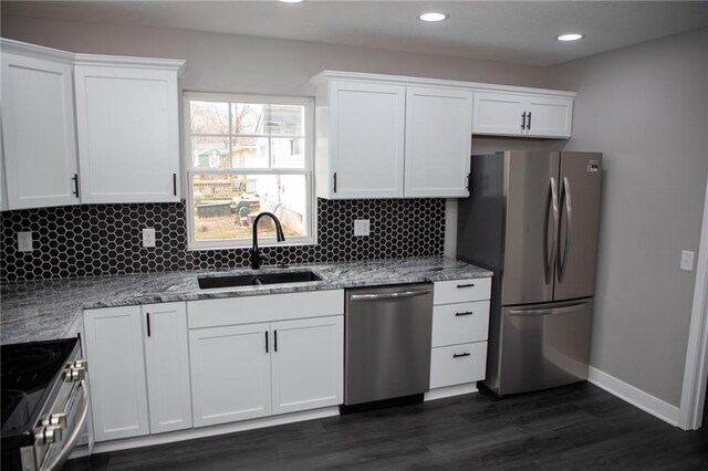 kitchen with appliances with stainless steel finishes, sink, white cabinets, decorative backsplash, and light stone countertops