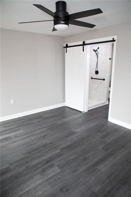 empty room with dark wood-type flooring, ceiling fan, and a barn door